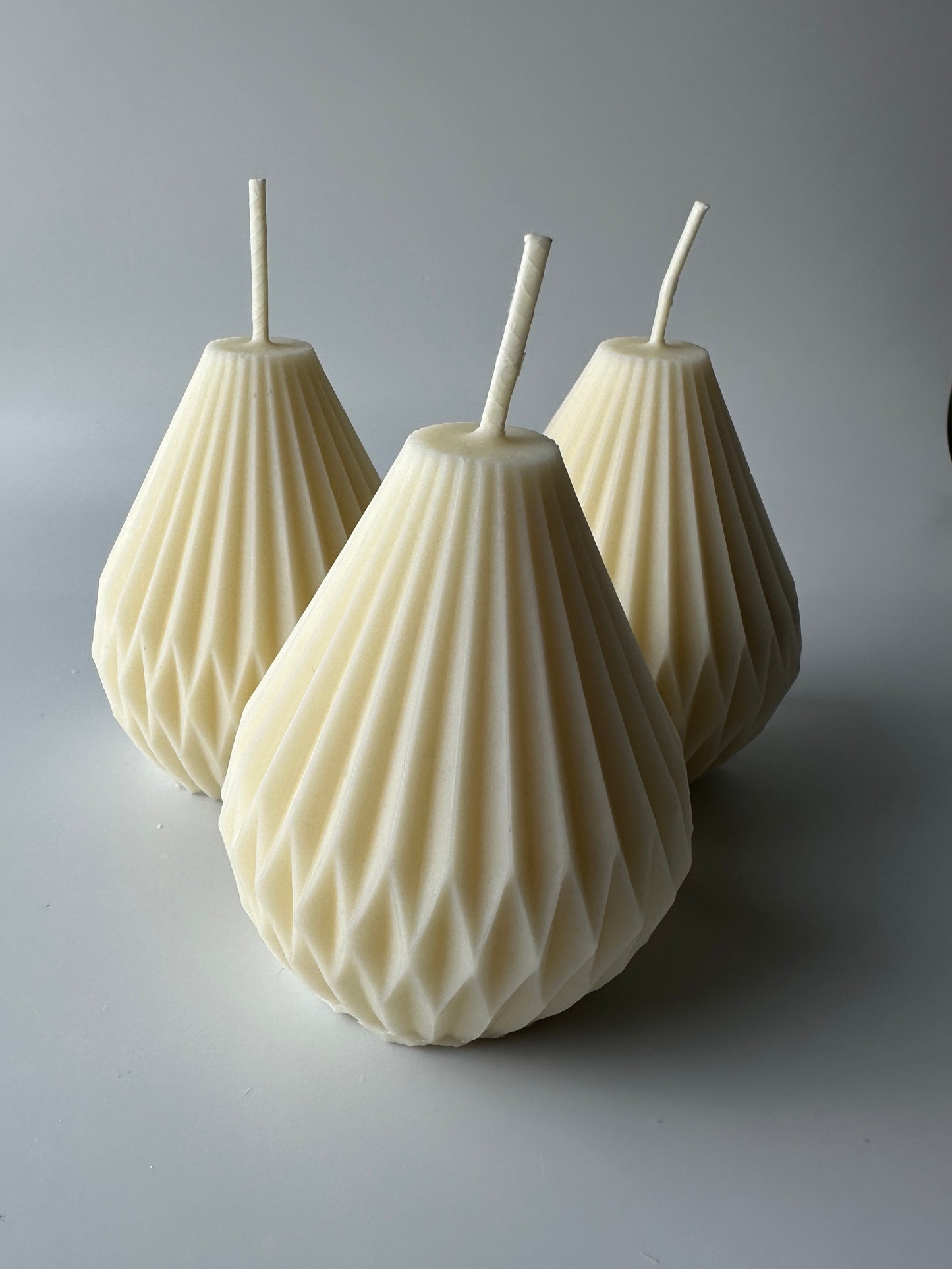 Dimensional candles are a type of pillar candle. A trio of natural unscented pear shaped geometric pillar candles is shown.