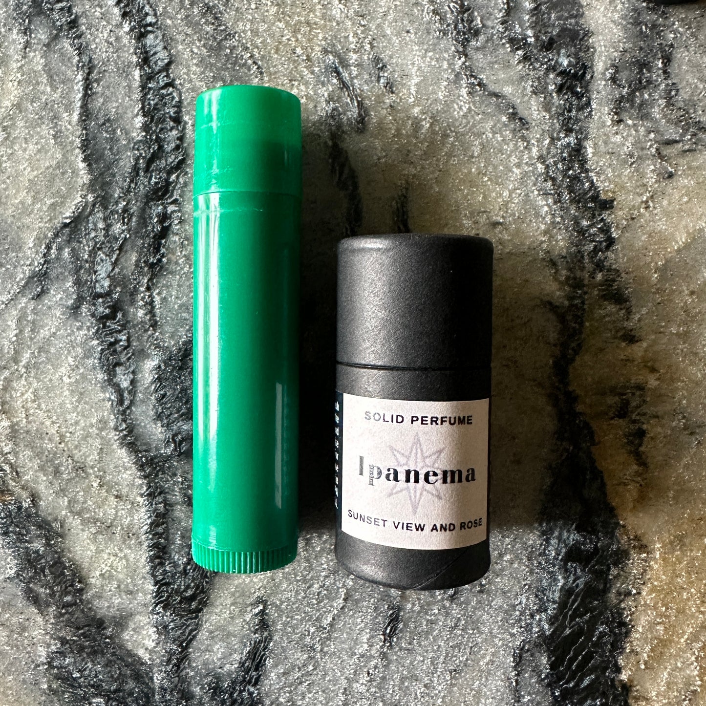 Green and black solid perfume containers on a textured surface